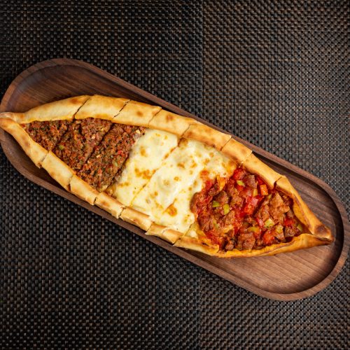 pide with stuffed meat cheese and pieces of fried meat on a wooden bowl