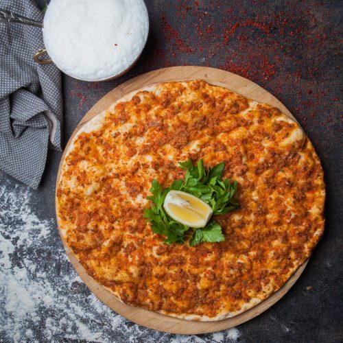 Top view lahmacun with parsley and lemon and ayran and rag in wooden food tray on stone background